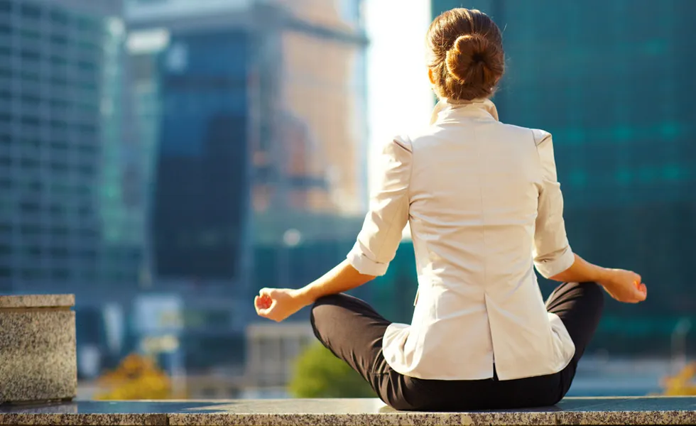 View from behind of a female relaxing in meditation looking at office buidings from an office balcony.